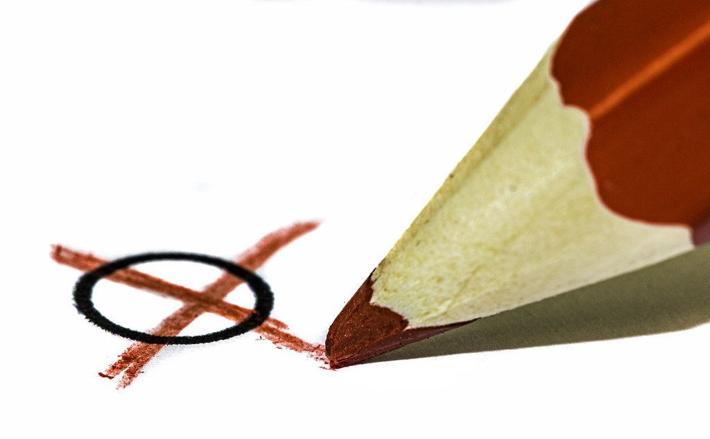 Ein roter Stift, der ein Kreuz auf ein weißes Blatt macht.